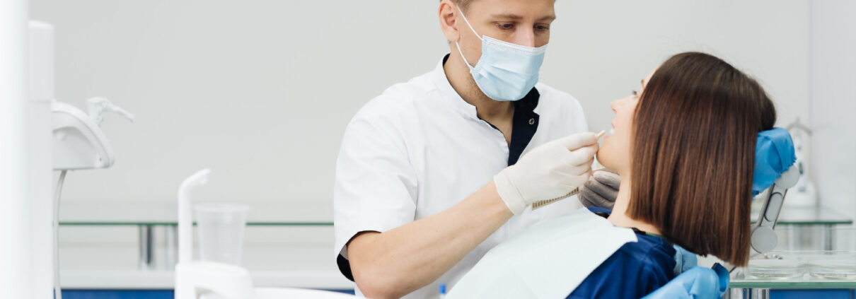 close-up-portrait-beautiful-young-lady-sitting-dental-chair-while-stomatologist-hands-sterile-gloves-holding-tooth-samples